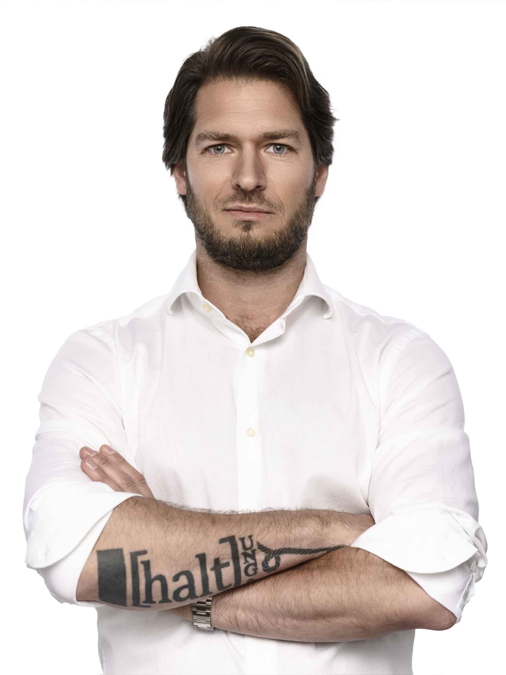 Alex Volz mit Tättowierung vor weißer Wand